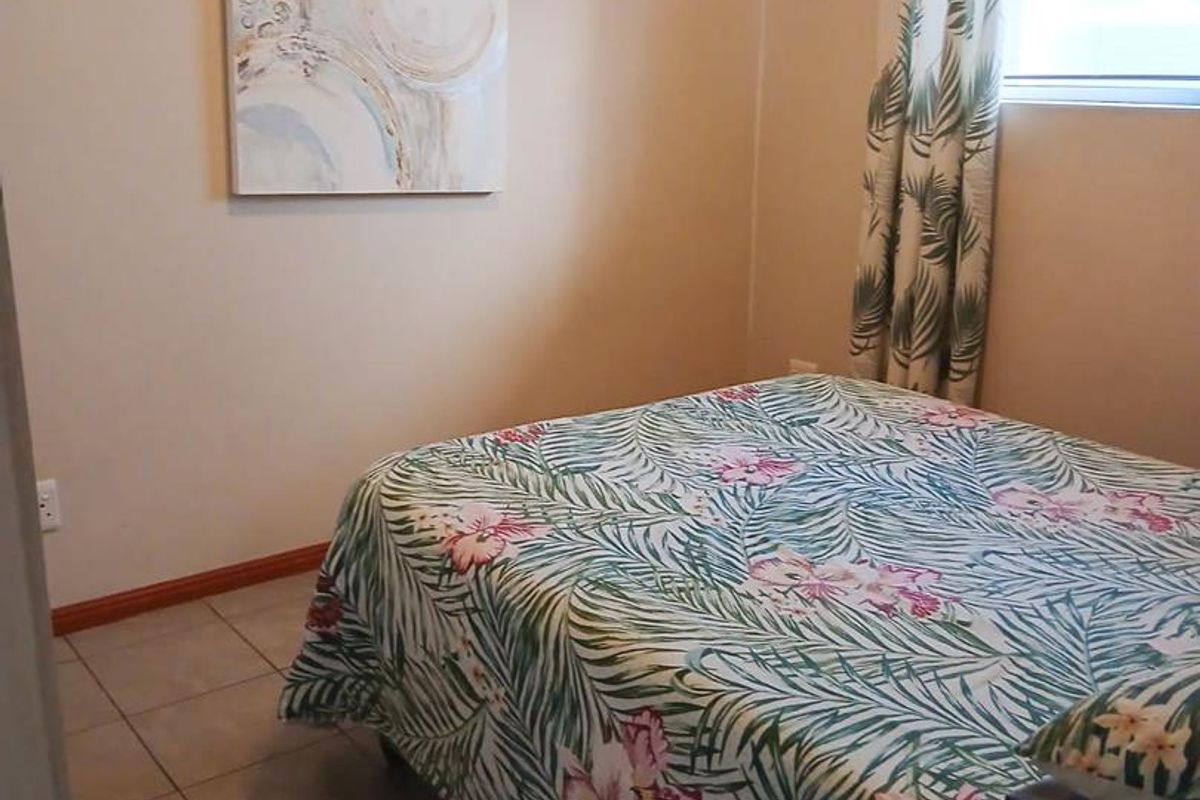 A bedroom featuring neutral wall tones, tiled flooring, and a window with curtain treatments.