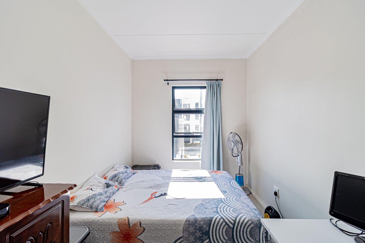 A compact bedroom featuring neutral walls, a central window with natural light, and standard electrical fixtures.