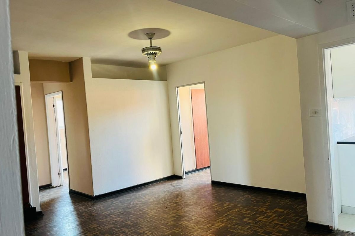 An empty living area featuring original parquet flooring, neutral walls, and a central ceiling fan, providing a blank canvas for interior design.