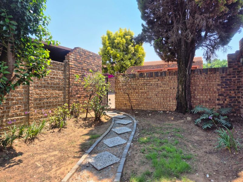 A private garden area featuring a brick boundary wall, a stone paver pathway, and established trees, providing a secure outdoor space.