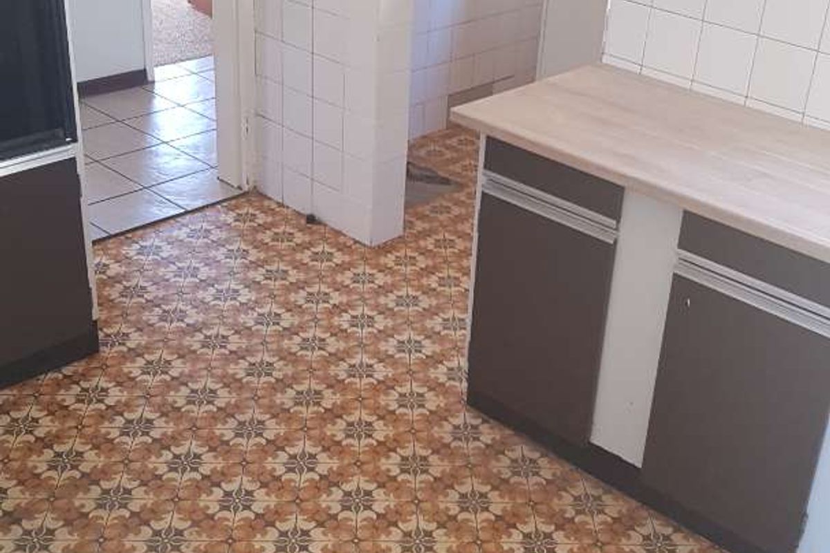 A dated kitchen featuring original patterned vinyl flooring, laminate countertops, and built-in cabinetry, offering significant potential for a modern renovation.