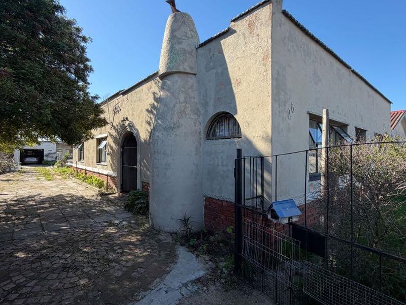 Front elevation of a character home featuring a distinctive chimney, arched architectural details, and a paved driveway leading to a rear garage.