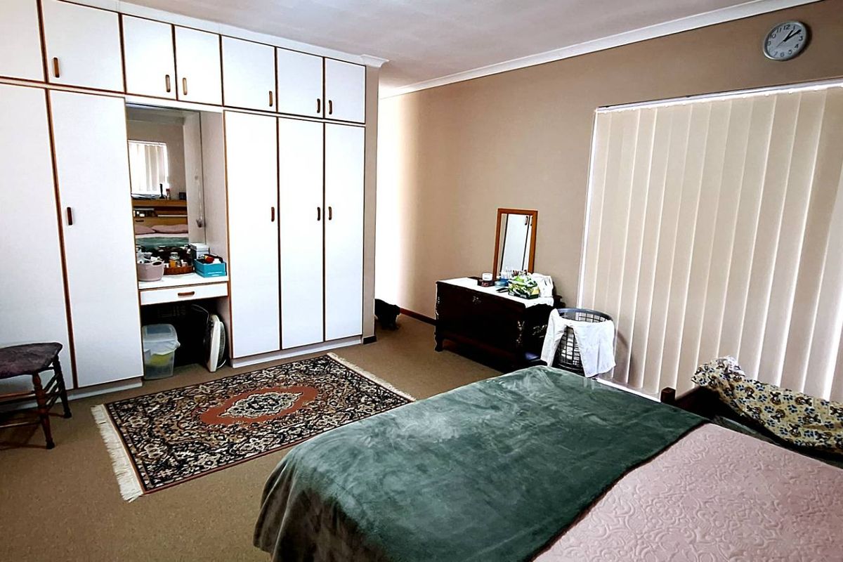A spacious bedroom featuring extensive built-in floor-to-ceiling cabinetry with an integrated vanity and large vertical blinds covering the window.