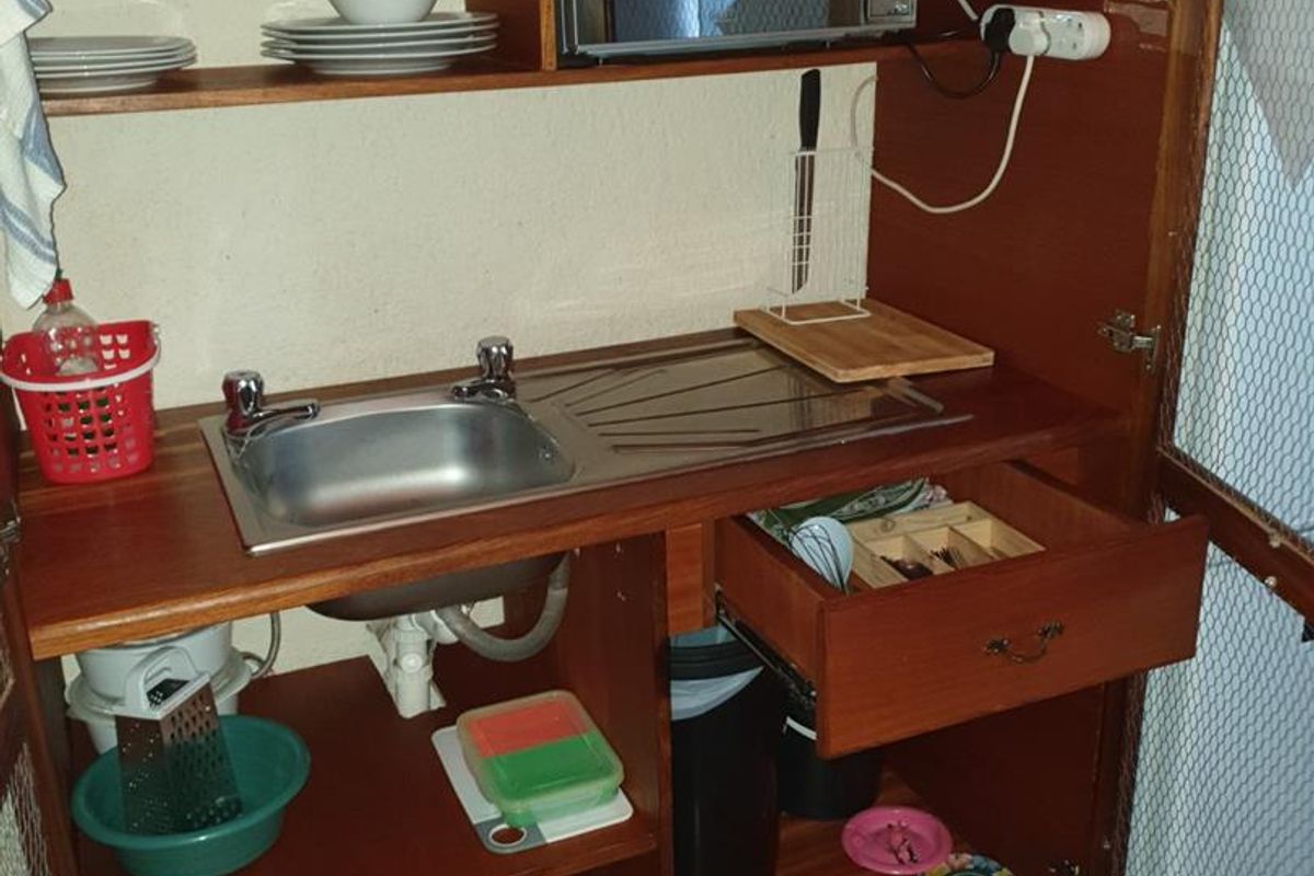 A compact kitchenette unit featuring a built-in stainless steel sink, wooden cabinetry, and an integrated microwave shelf.