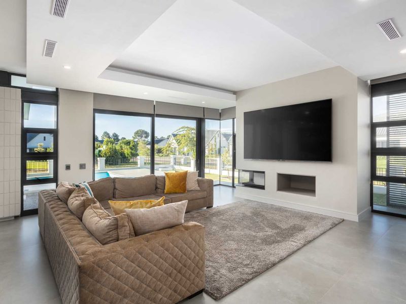 Modern living room featuring large format floor tiles, recessed ceiling with ducted air conditioning, and expansive sliding glass doors overlooking the pool area.