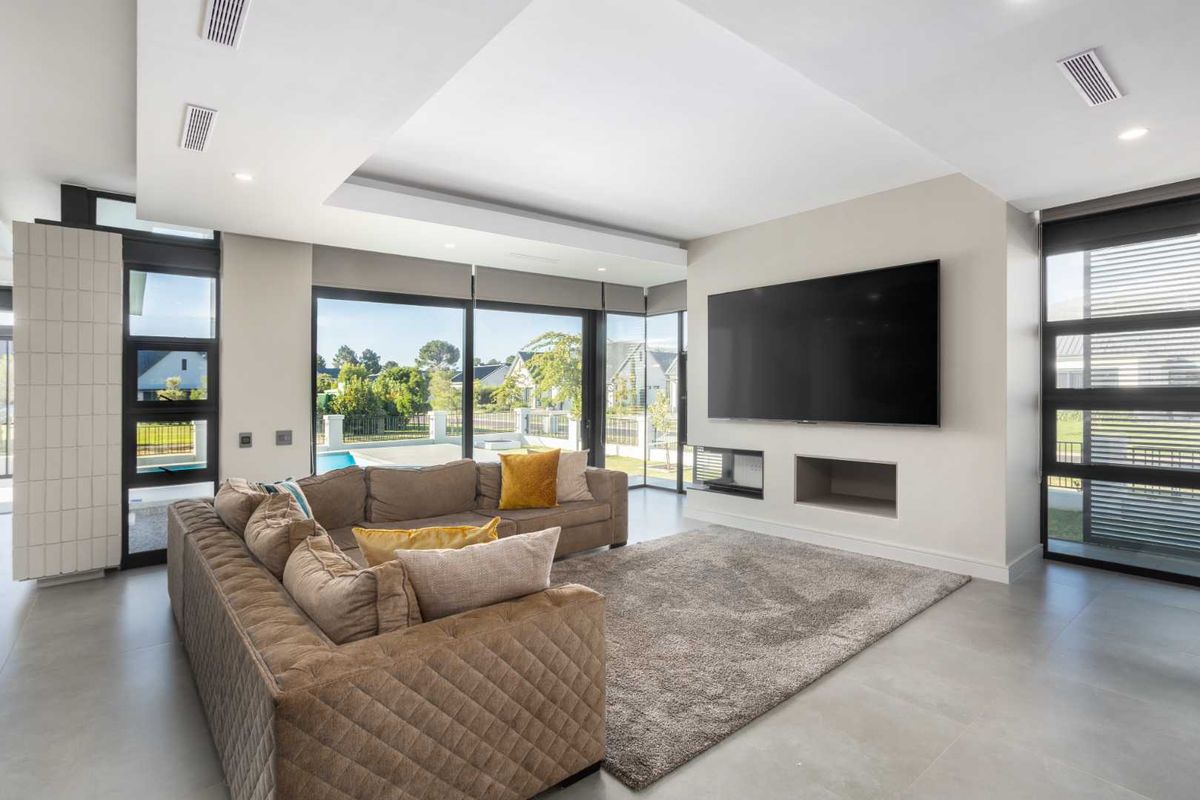 Modern living room featuring large format floor tiles, recessed ceiling with ducted air conditioning, and expansive sliding glass doors overlooking the pool area.