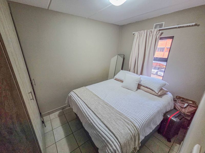 A compact bedroom featuring tiled flooring, a built-in wardrobe, and a window with a curtain rail.