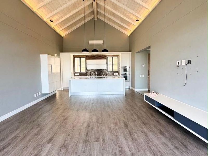 Spacious open-plan living and kitchen area featuring a high vaulted timber ceiling, modern cabinetry, kitchen island, and durable laminate flooring.