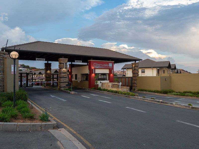 The secure entrance to Glenvale complex featuring a manned gatehouse, boom gates, stone-clad pillars, and well-maintained paved access roads.