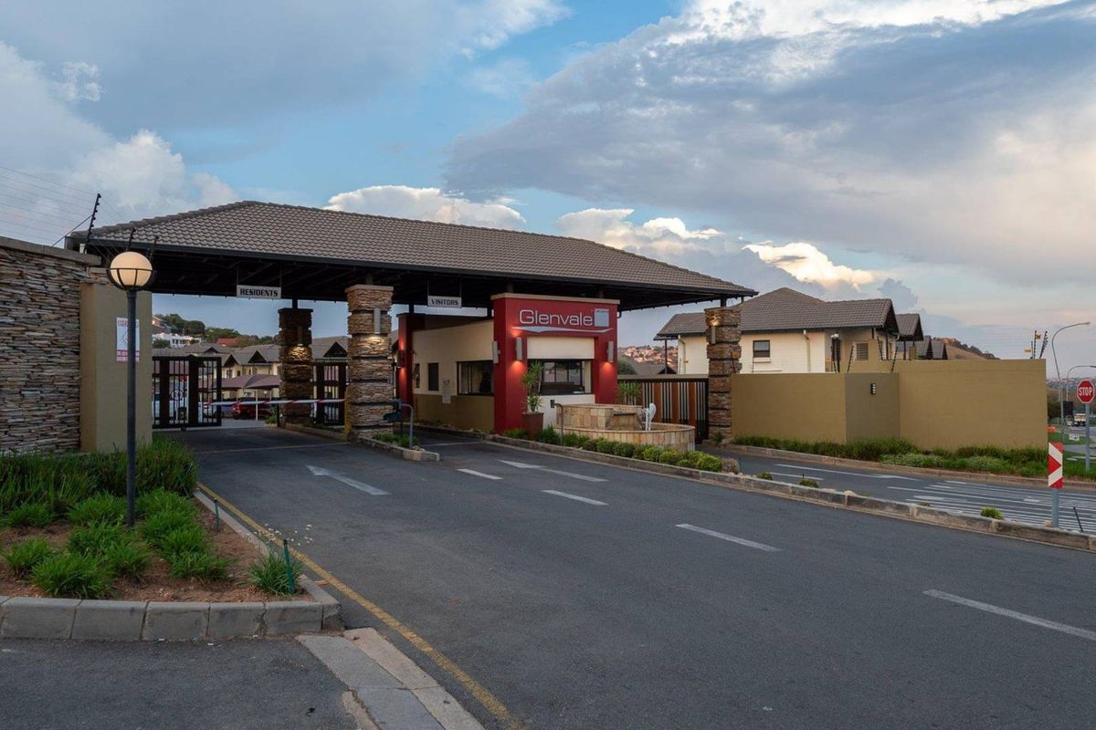 The secure entrance to Glenvale complex featuring a manned gatehouse, boom gates, stone-clad pillars, and well-maintained paved access roads.
