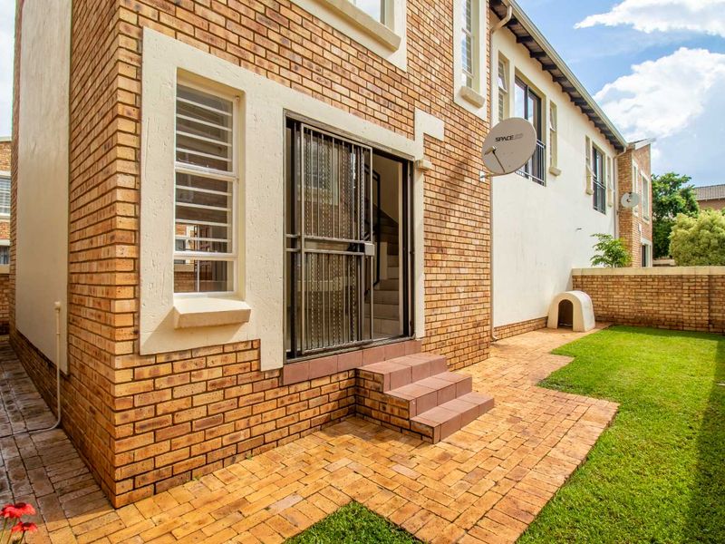 Rear view of the townhouse featuring a brick facade, paved patio area, and a private garden with a brick boundary wall.