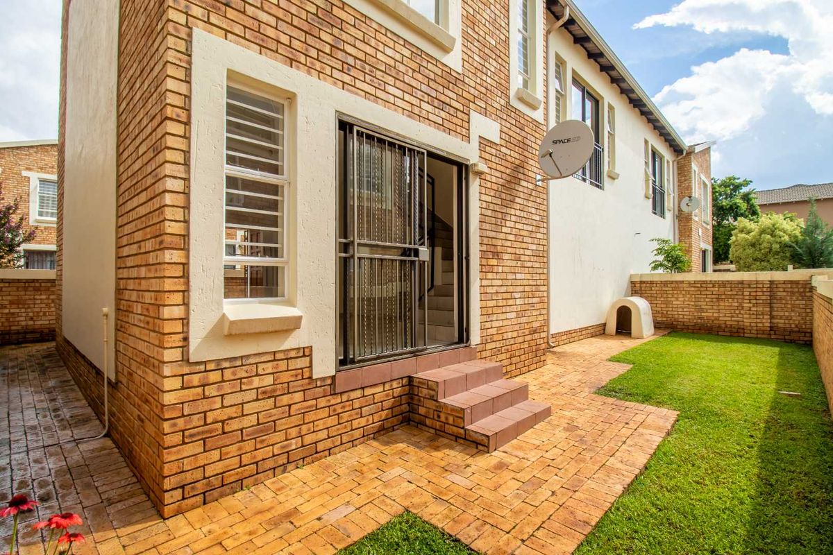 Rear view of the townhouse featuring a brick facade, paved patio area, and a private garden with a brick boundary wall.