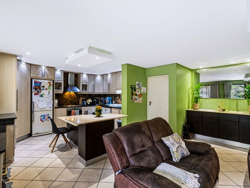Open-plan living and kitchen area featuring tiled flooring, built-in cabinetry, and a central kitchen island, offering a functional layout for daily living.