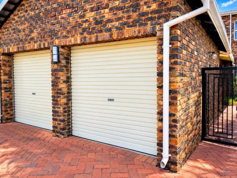 A well-maintained double garage featuring face brick construction, cream-colored roller doors, and a paved driveway with an adjacent security gate.