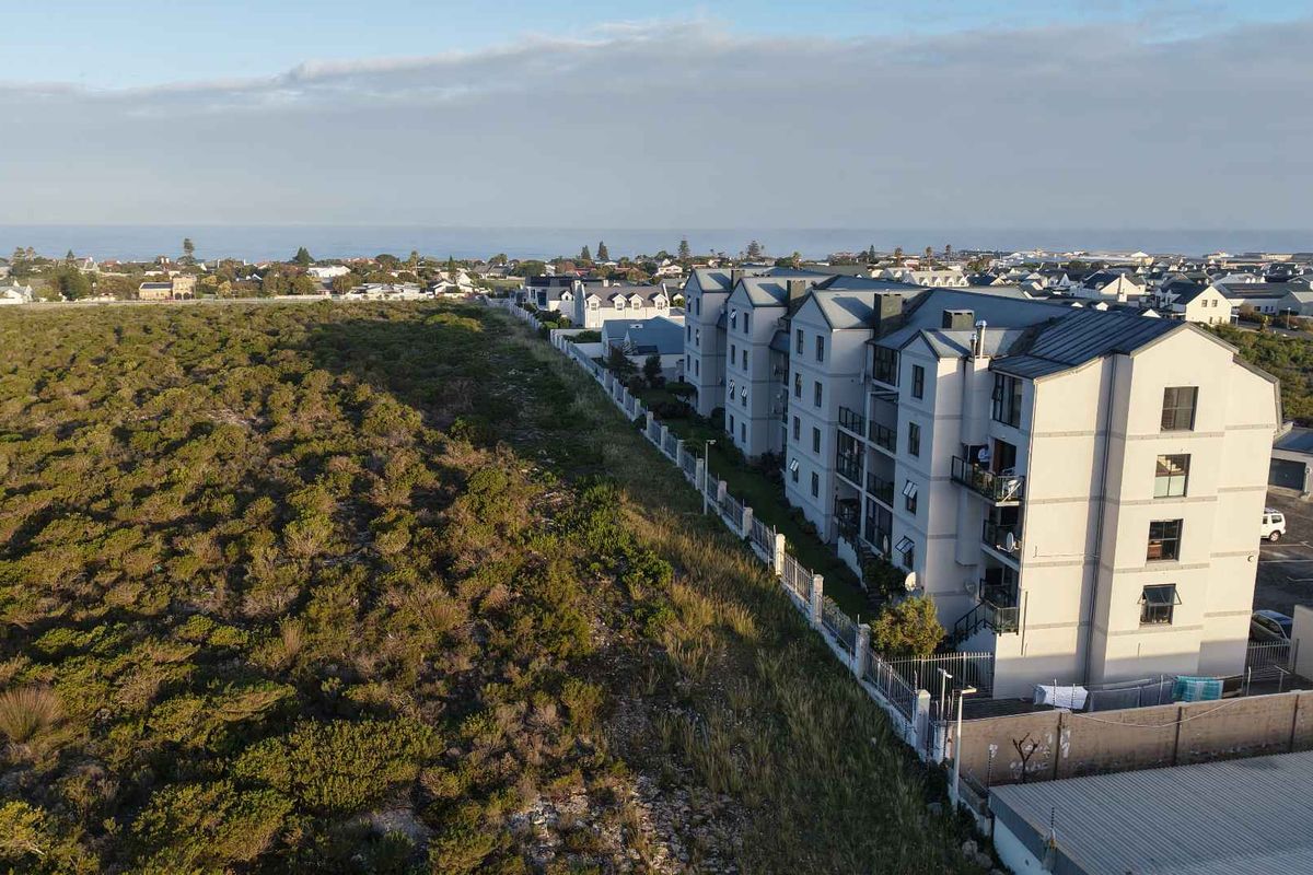 Aerial view of a multi-story apartment complex situated near coastal vegetation and residential neighborhood.