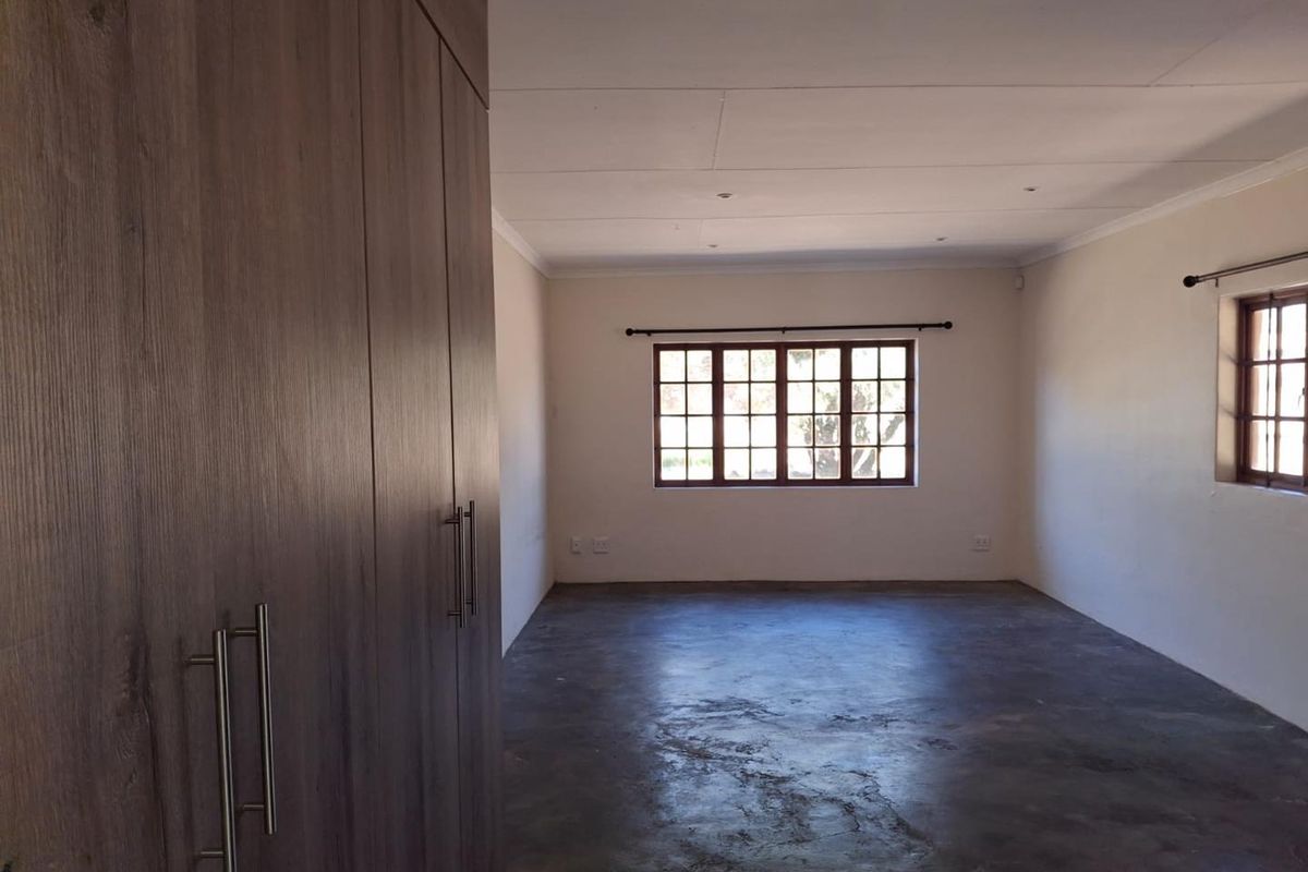 An empty bedroom featuring built-in cupboards, concrete flooring, and wooden-framed windows, offering a blank canvas for personalization.