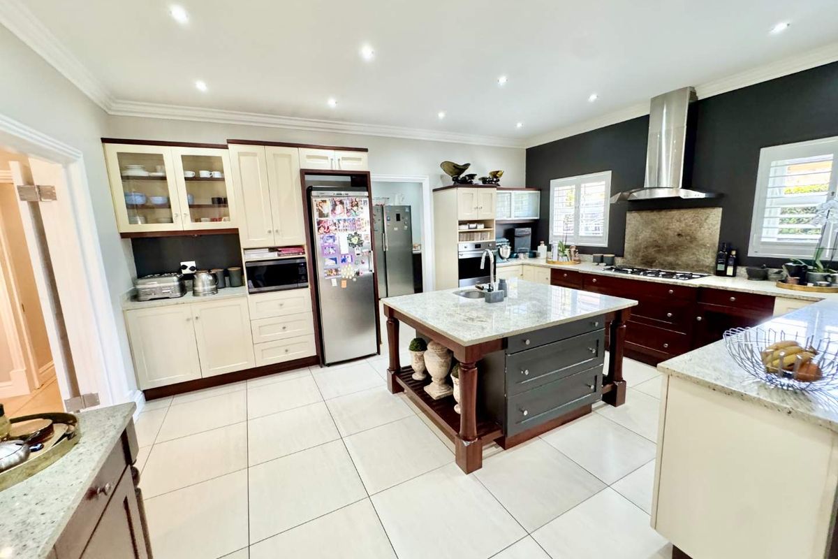 Spacious kitchen featuring a central island with stone countertops, built-in cabinetry, stainless steel extractor fan, and tiled flooring.