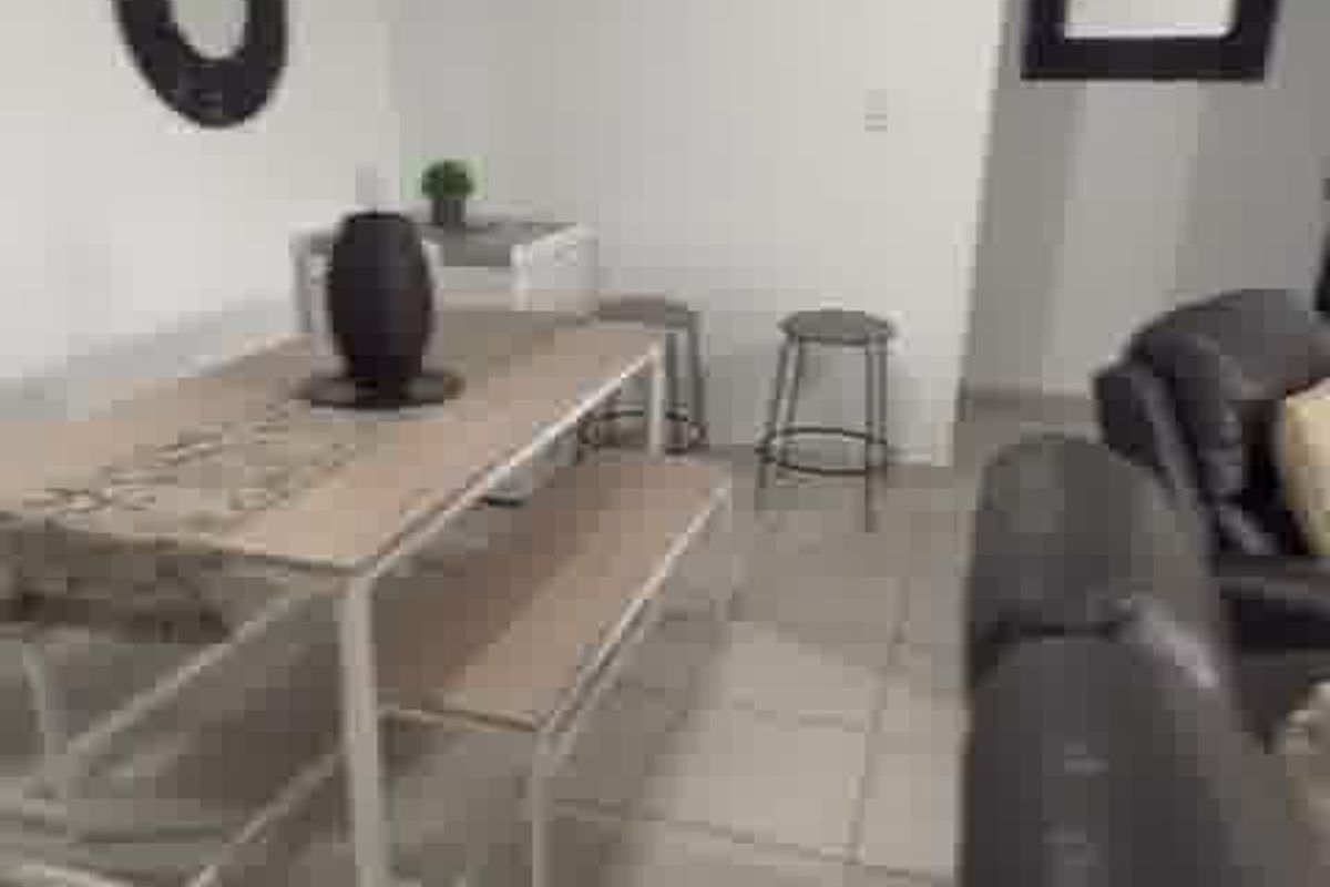An open-plan living and dining area featuring neutral ceramic floor tiles and a simple, functional layout.