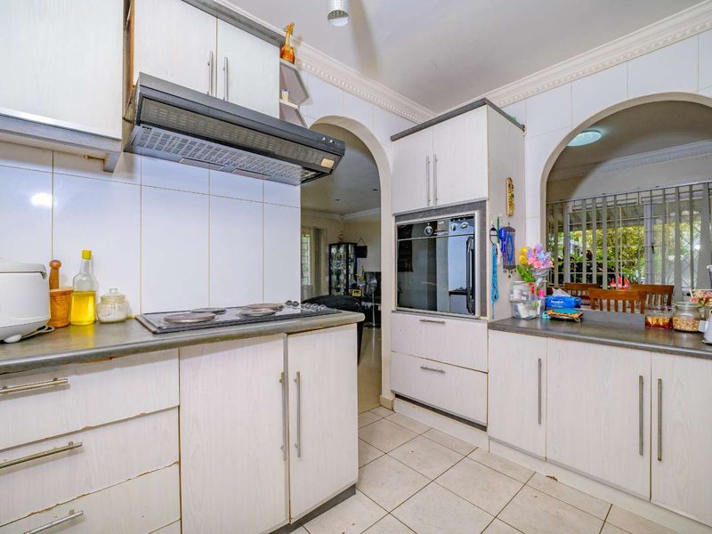 A functional kitchen featuring built-in cabinetry, an integrated oven, electric hob, and tiled finishes, offering a practical layout with an open archway design.