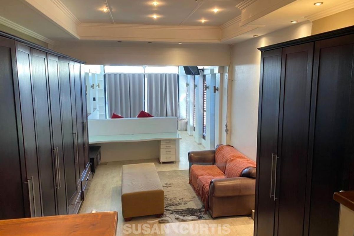 A spacious living area featuring extensive built-in dark wood cabinetry, recessed ceiling lighting, and a functional desk workspace.