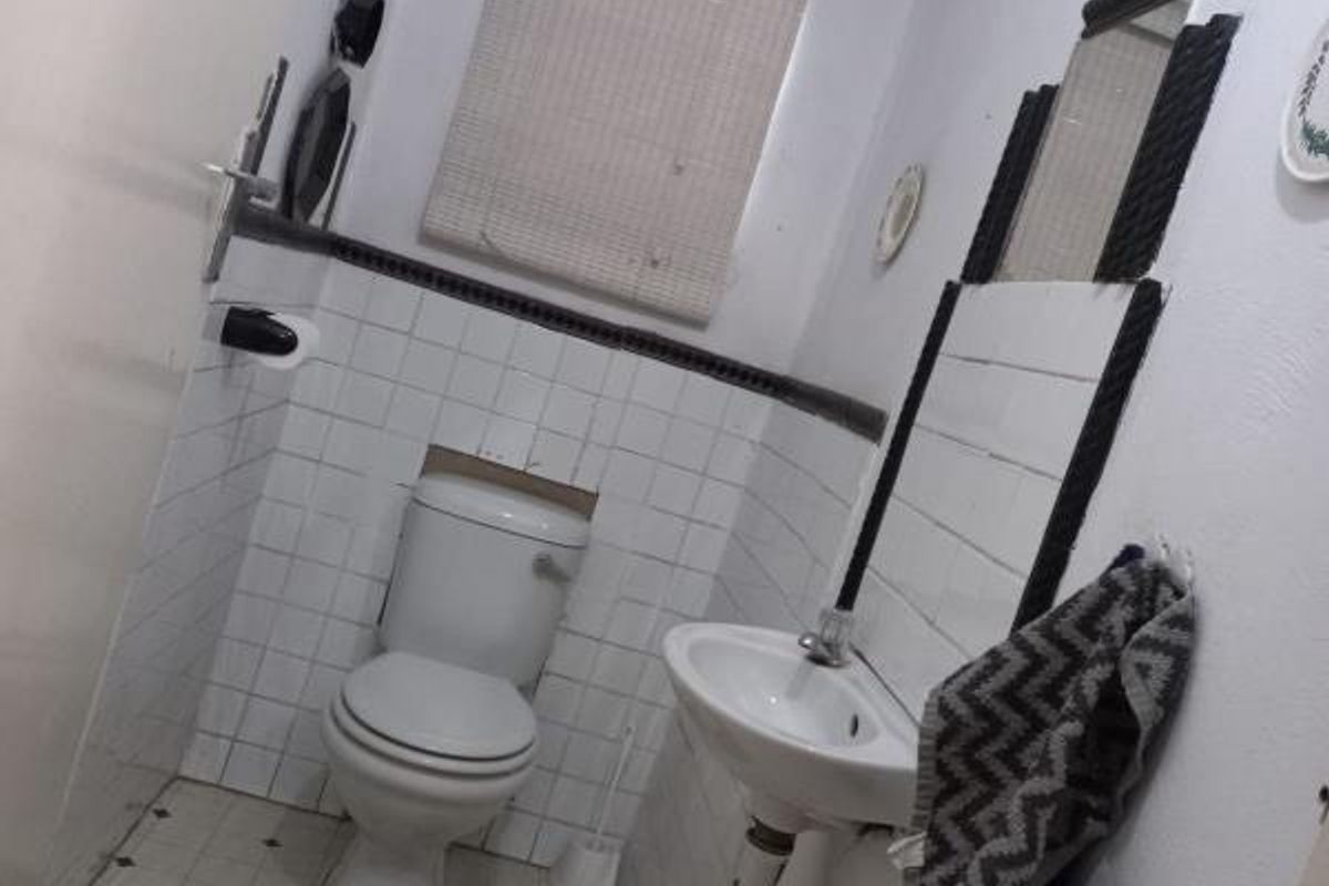 A compact bathroom featuring a standard toilet and pedestal basin with tiled splashbacks and a window blind.