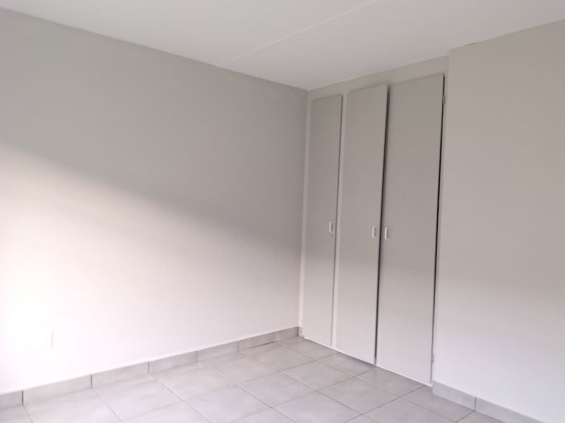 A clean, empty bedroom featuring neutral wall paint, tiled flooring, and built-in cupboards.