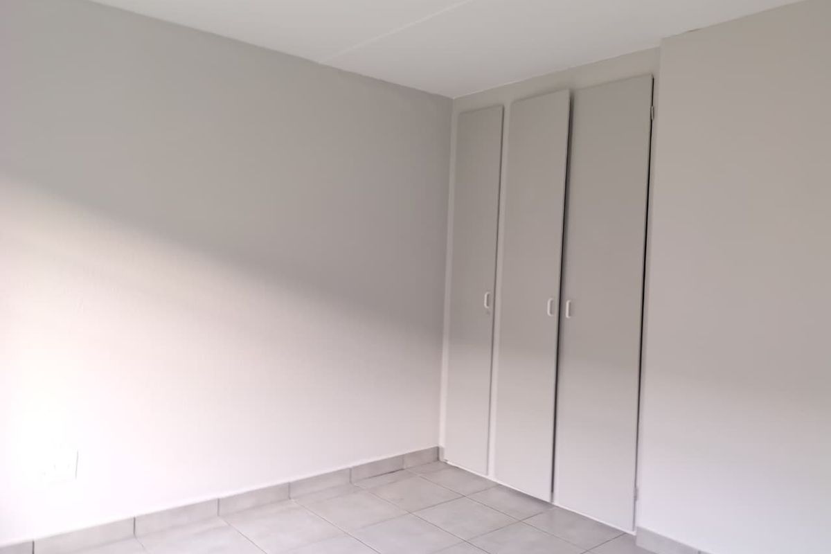 A clean, empty bedroom featuring neutral wall paint, tiled flooring, and built-in cupboards.