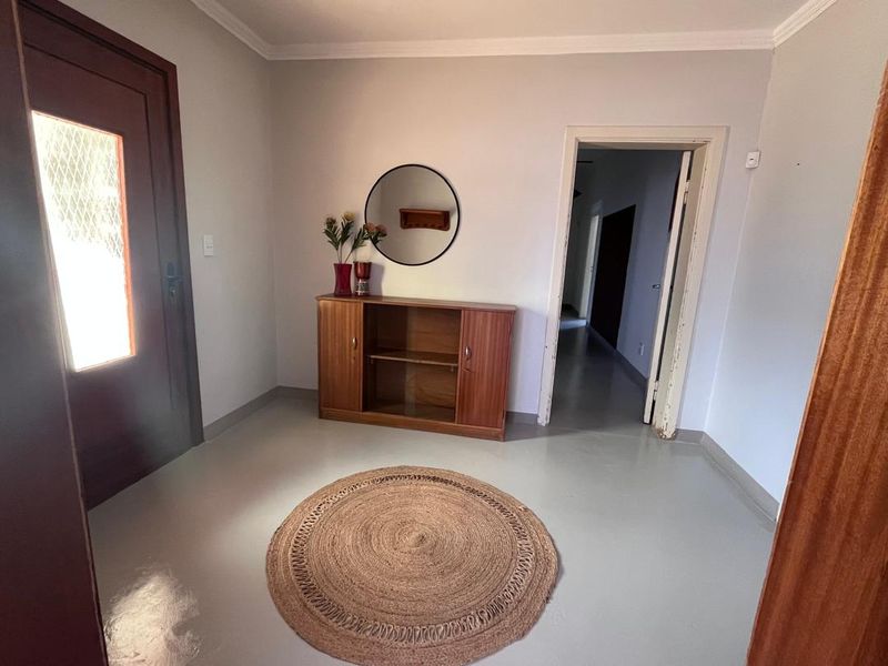 A bright and functional entrance hall featuring a timber front door, neutral painted walls, and durable concrete flooring, leading into the home's interior hallway.
