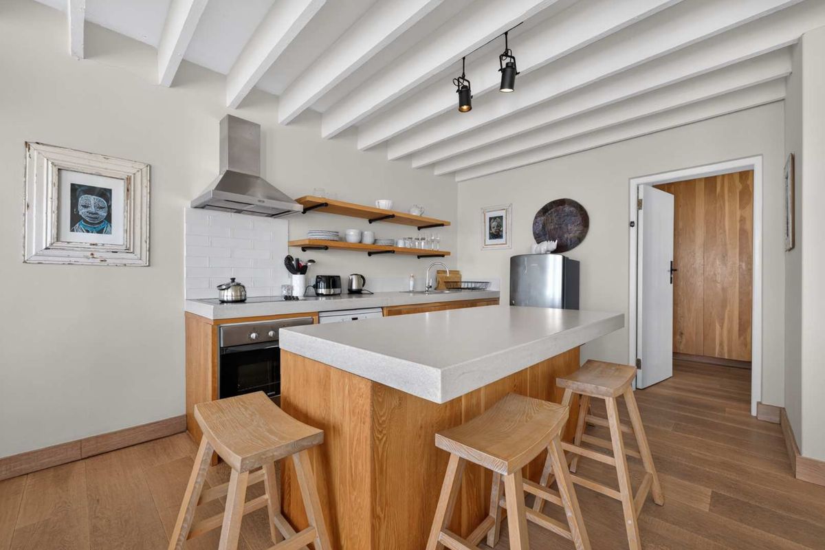 Modern kitchen featuring a central island with stone countertop, exposed beam ceiling, open shelving, and high-quality hardwood flooring.