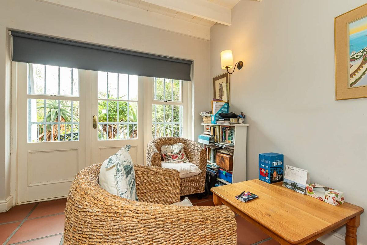 A cozy living area featuring terracotta floor tiles, exposed beam ceiling, and double doors with security bars providing access to the garden.