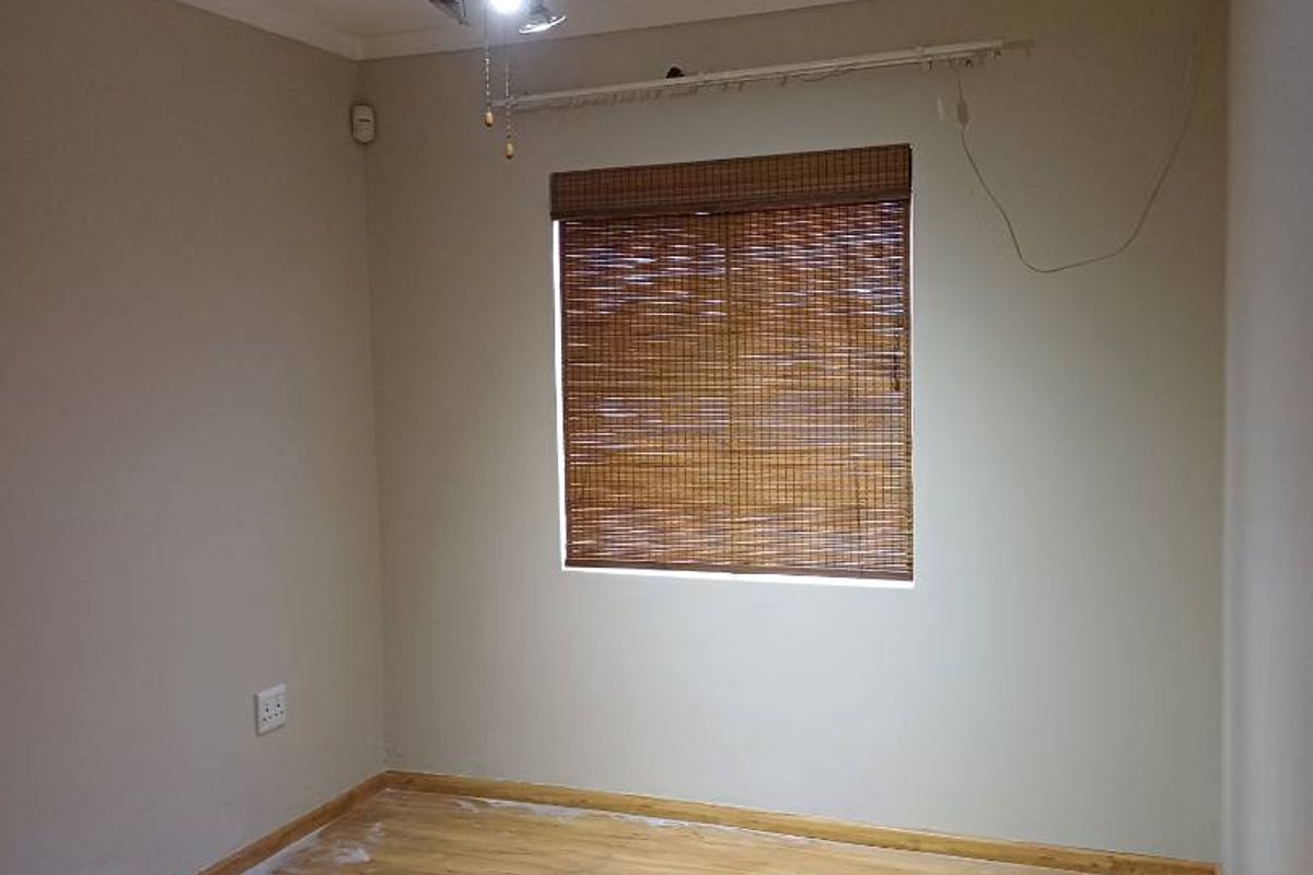 A vacant bedroom featuring light wood-look flooring, neutral walls, a ceiling fan, and a window fitted with a bamboo blind.