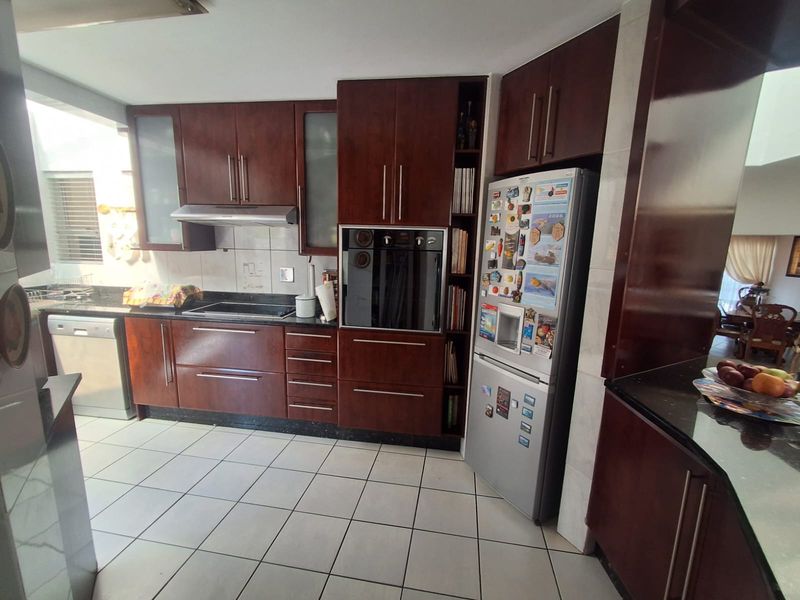 A functional kitchen featuring dark wood cabinetry, granite countertops, built-in oven, electric hob, and tiled flooring, offering a classic and practical workspace.