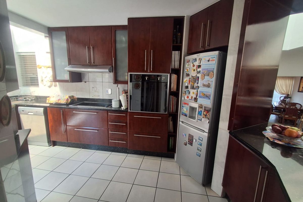 A functional kitchen featuring dark wood cabinetry, granite countertops, built-in oven, electric hob, and tiled flooring, offering a classic and practical workspace.