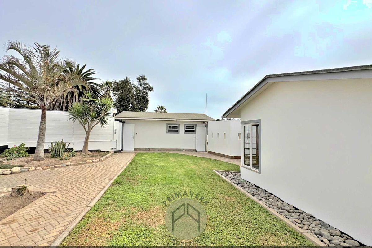 A well-maintained rear garden area featuring a paved walkway, a central lawn, and a detached outbuilding with white exterior walls.
