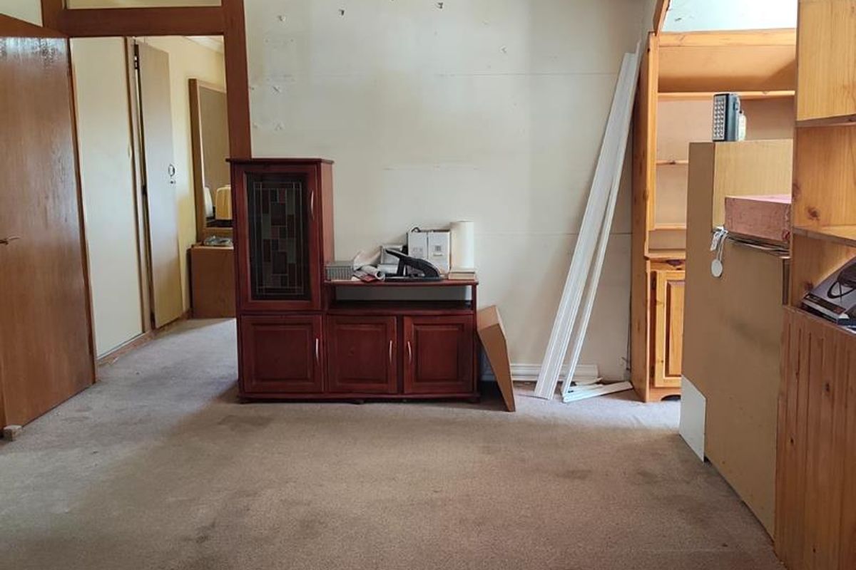 A dated living room featuring timber ceiling beams, built-in shelving, and worn carpeting, offering significant potential for renovation and modernization.