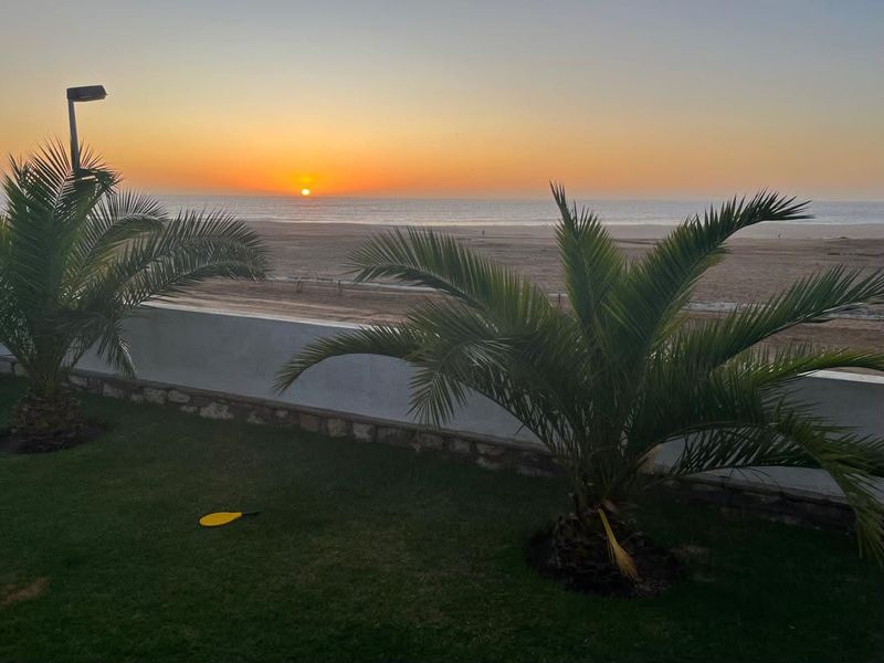 A scenic sunset view overlooking the beach, featuring a well-maintained garden lawn and a low boundary wall.