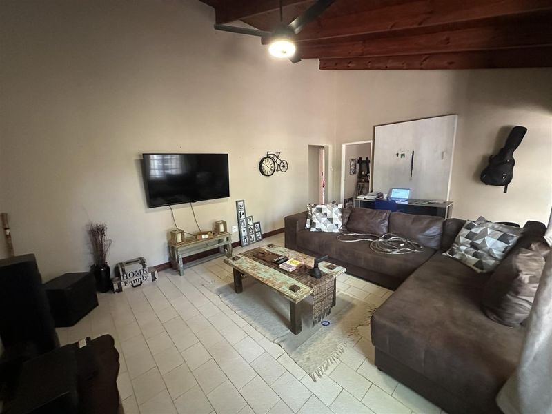 Spacious living room featuring exposed timber ceiling beams, a ceiling fan, and neutral tiled flooring, offering a comfortable and functional layout.