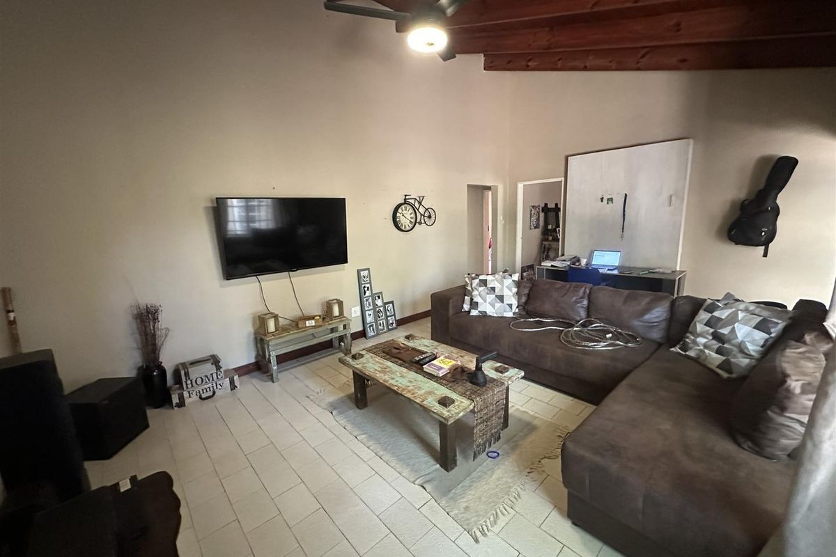 Spacious living room featuring exposed timber ceiling beams, a ceiling fan, and neutral tiled flooring, offering a comfortable and functional layout.