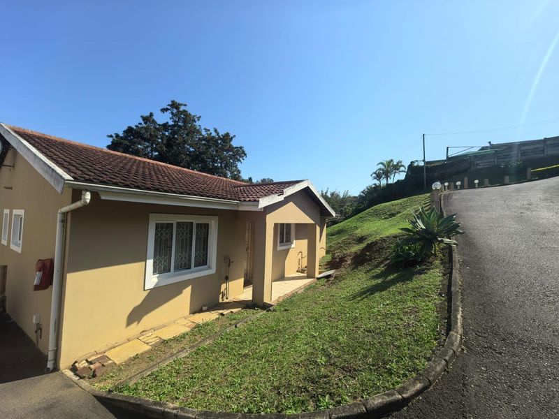 Exterior view of a townhouse featuring a tiled roof, security-barred windows, and a paved driveway with adjacent lawn area.