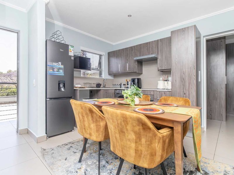 An open-plan living and kitchen area featuring modern wood-grain cabinetry, tiled flooring, and direct access to an outdoor balcony.