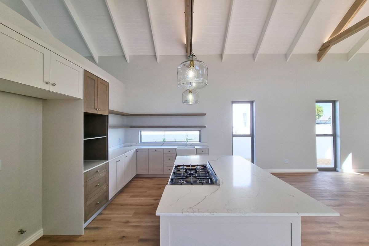 Modern open-plan kitchen featuring a large central island with a built-in gas hob, stone countertops, and high vaulted ceilings with exposed beams.