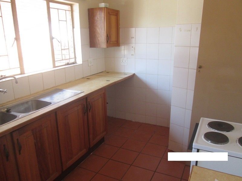 A functional kitchen featuring wooden cabinetry, tiled backsplash, and tiled flooring, offering a blank canvas for potential modern updates and renovation.