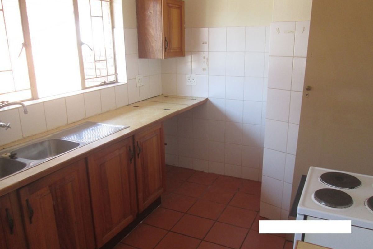 A functional kitchen featuring wooden cabinetry, tiled backsplash, and tiled flooring, offering a blank canvas for potential modern updates and renovation.