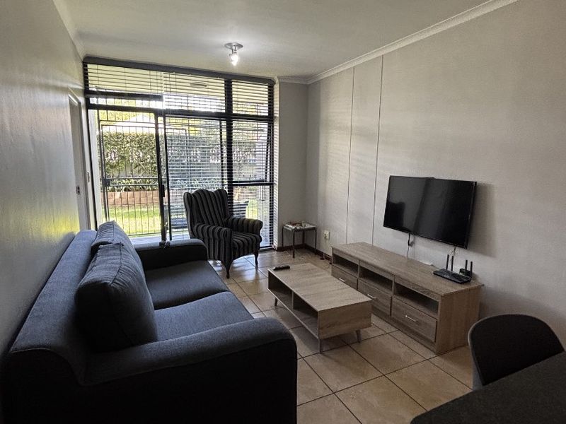 A living room featuring tiled flooring and a large sliding glass door with security gate, providing access to the outdoor area.