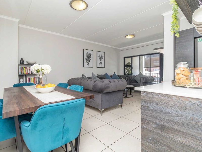 An open-plan living and dining area featuring tiled flooring, modern kitchen cabinetry with stone countertops, and access to a balcony through sliding glass doors.