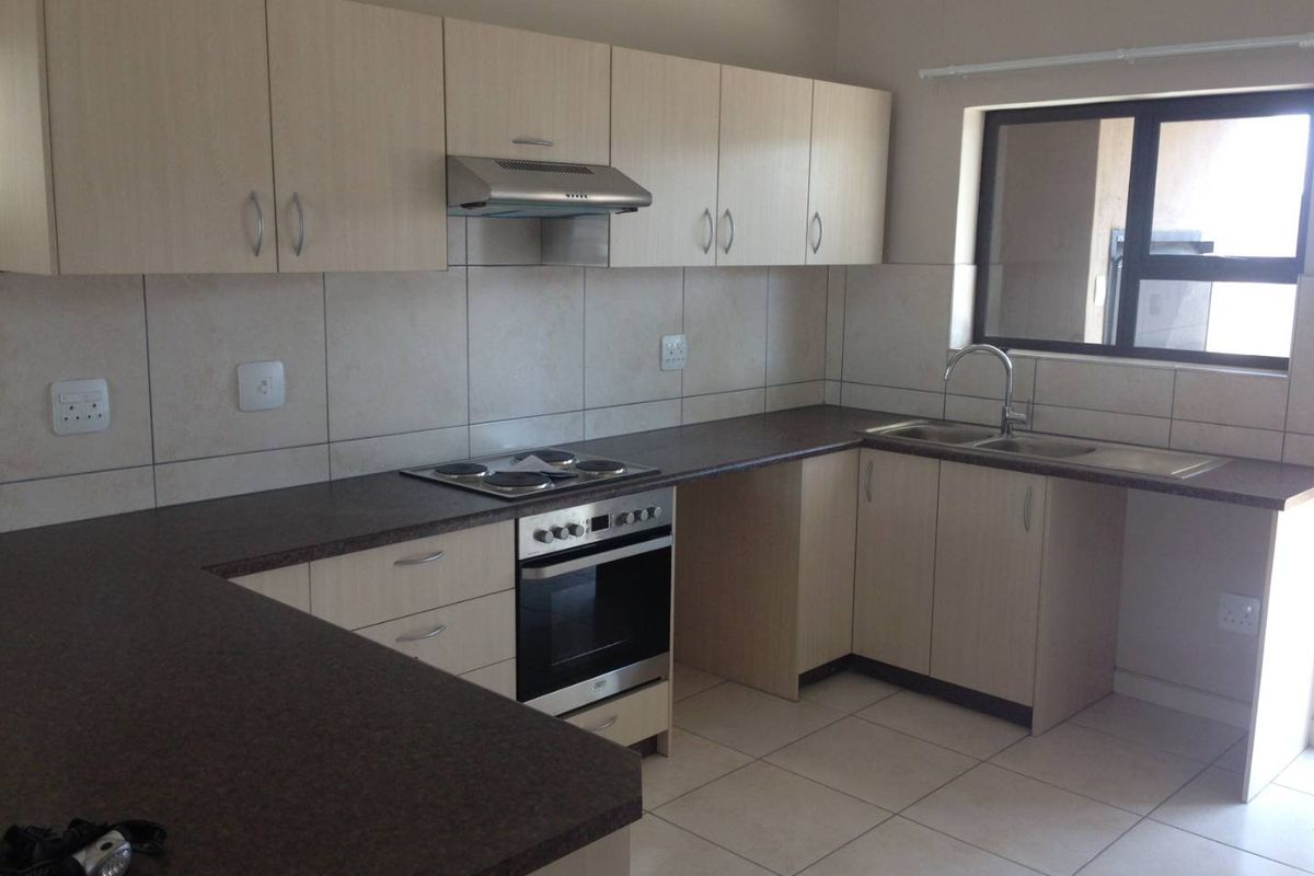 A clean, functional kitchen featuring light wood-tone cabinetry, dark laminate countertops, built-in oven, electric hob, and tiled finishes throughout.