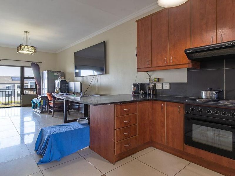 Open-plan living area featuring a kitchen with wood-finish cabinetry, granite countertops, and integrated appliances, leading to a balcony with natural light.