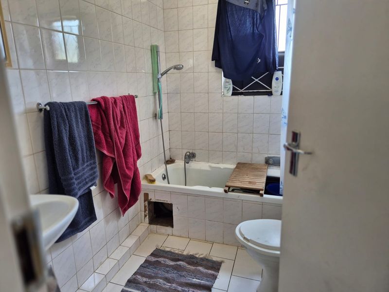 A functional bathroom featuring a bathtub with handheld shower, pedestal basin, and toilet, finished with ceramic wall and floor tiles.