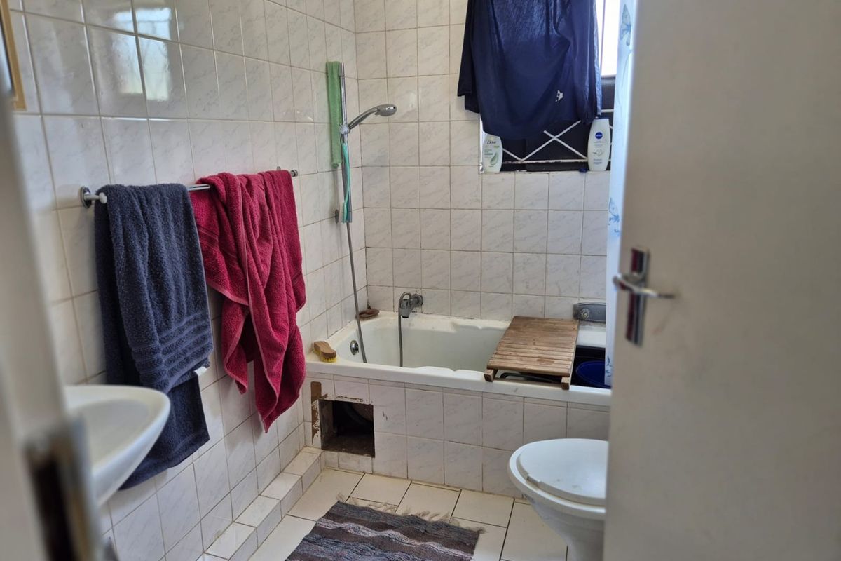 A functional bathroom featuring a bathtub with handheld shower, pedestal basin, and toilet, finished with ceramic wall and floor tiles.