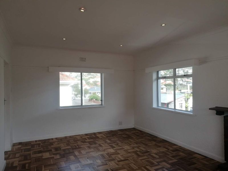 A bright, empty living room featuring classic parquet flooring, recessed downlighting, and large windows offering a pleasant neighborhood view.